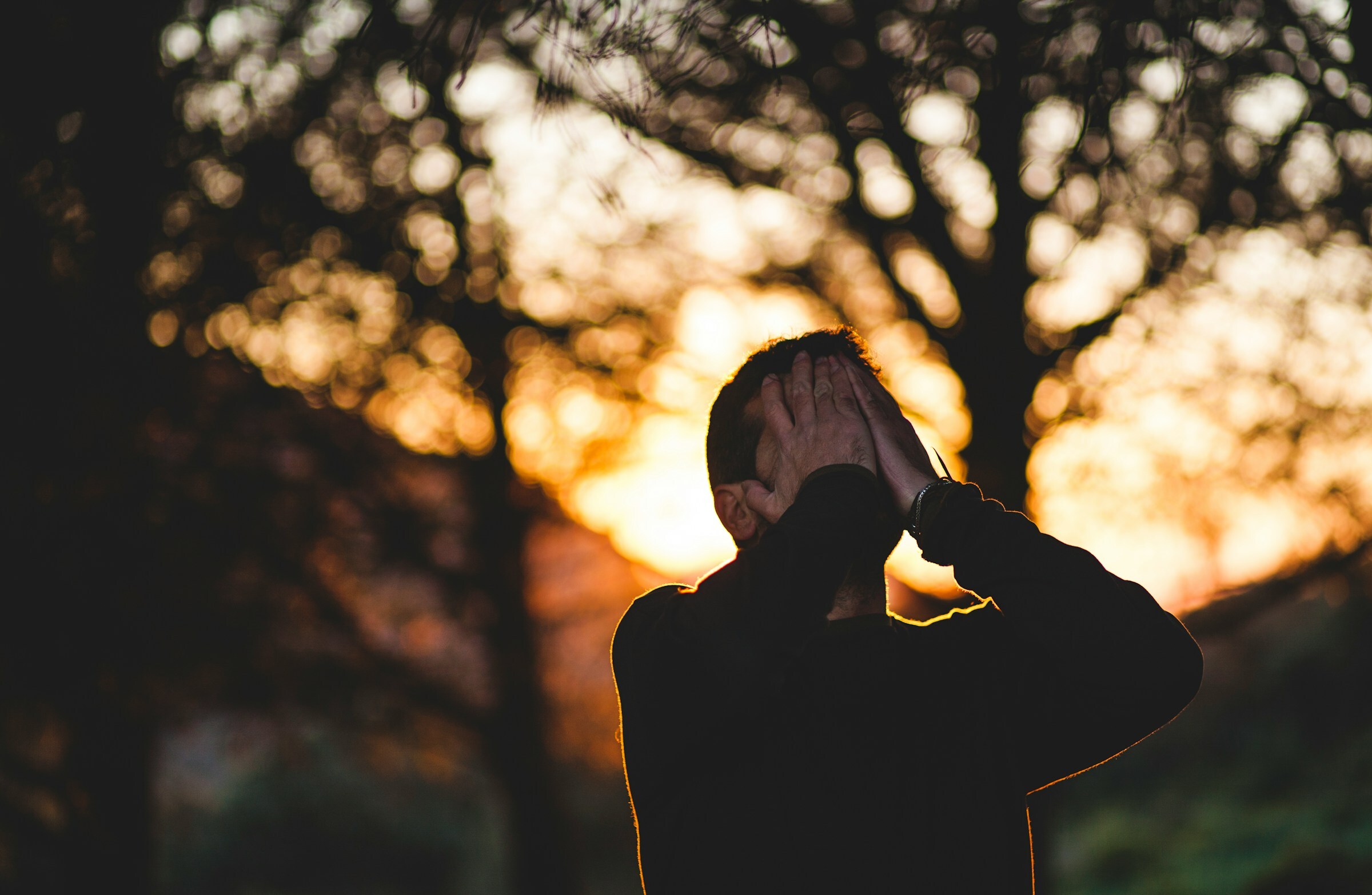 Man met handen voor zijn gezicht bij zonsondergang - Image: Unsplashed | Francisco Moreno